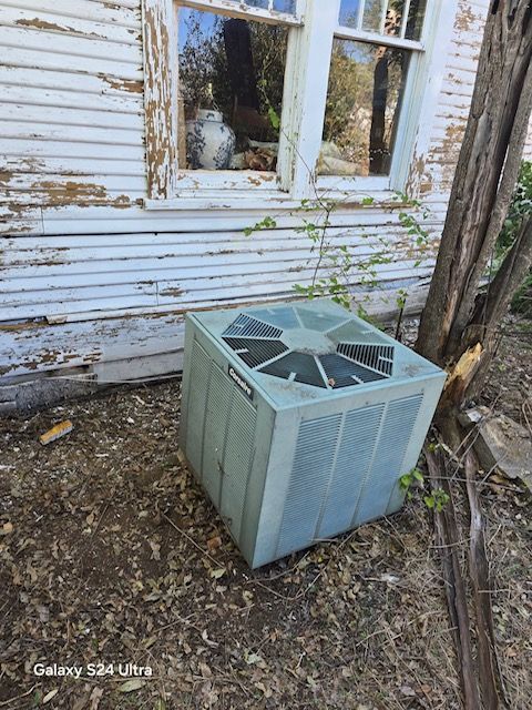 Air conditioning unit outside a weathered, white building with peeling paint.