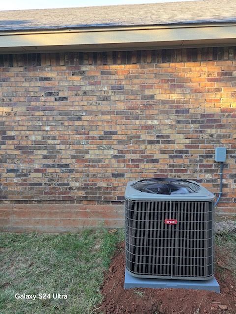 Air conditioner unit against a brick wall. The unit sits on a concrete pad with a dark, enclosed top.