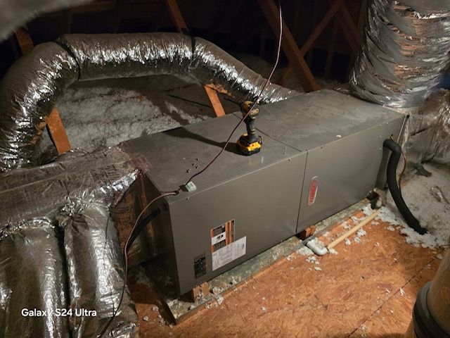 HVAC unit in an attic with ductwork and insulation; a cordless drill sits on top.