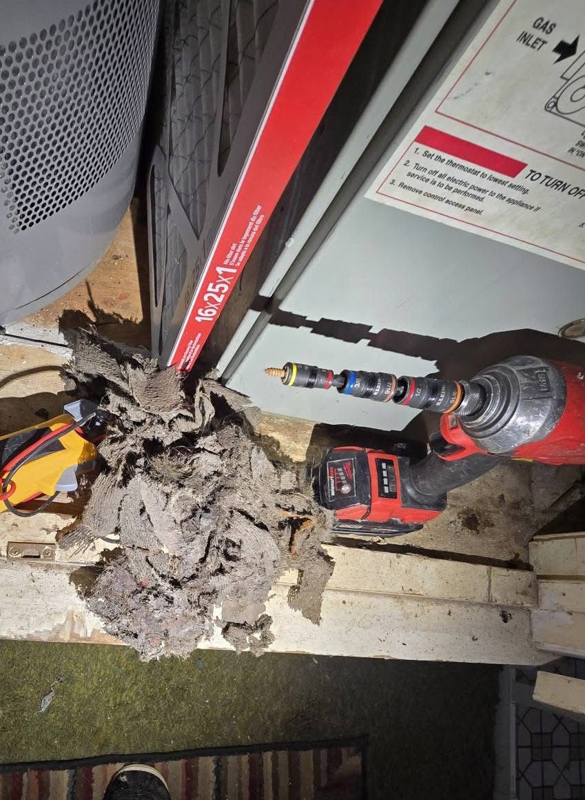 A dirty air filter being removed with a power drill from a furnace.