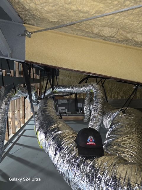 Furnace in a basement, with ductwork and pipes against a white wall. Gray floor.