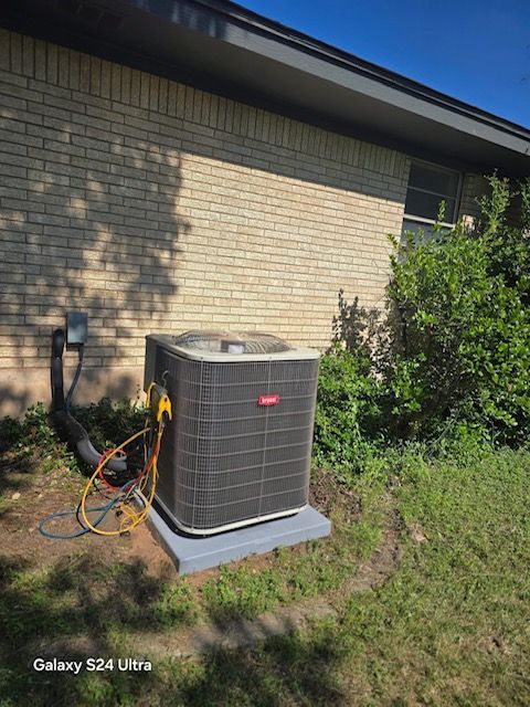 An HVAC unit, rectangular and beige, sits in an attic. Ductwork surrounds the unit.