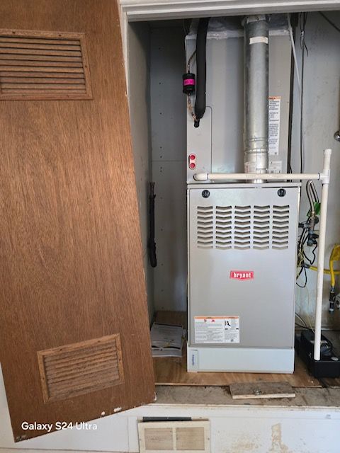 Furnace unit inside a utility closet, with vent and door open. Gray unit with vent pipes.