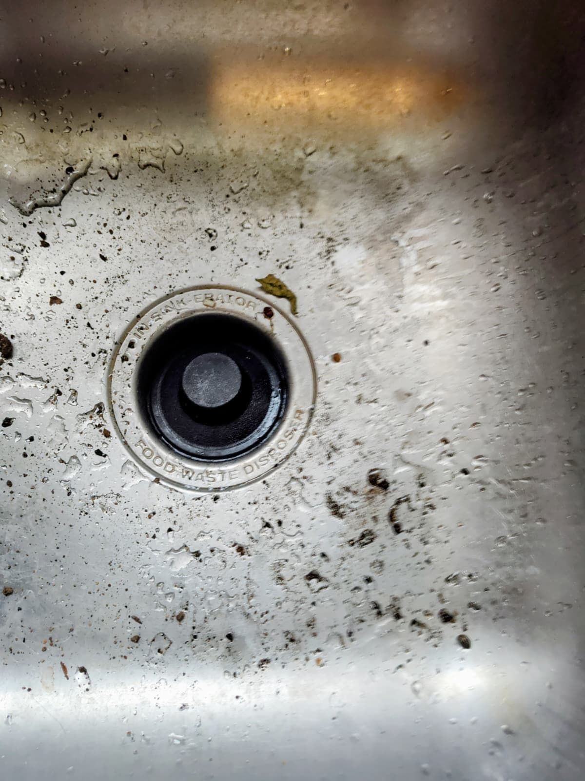 Dirty stainless steel sink drain with a black garbage disposal opening and stains around it
