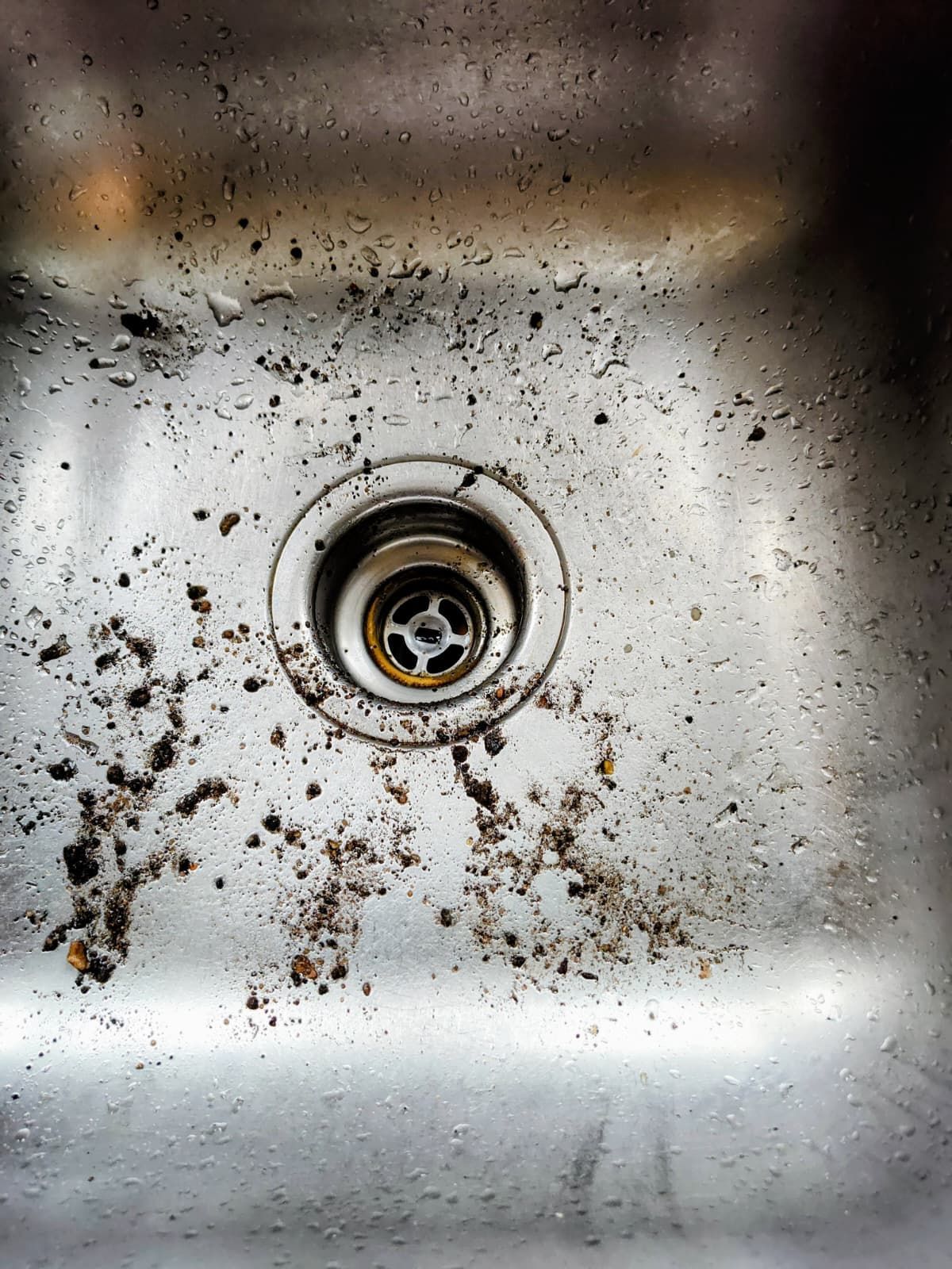 Dirty stainless steel sink drain with scattered grime and water stains