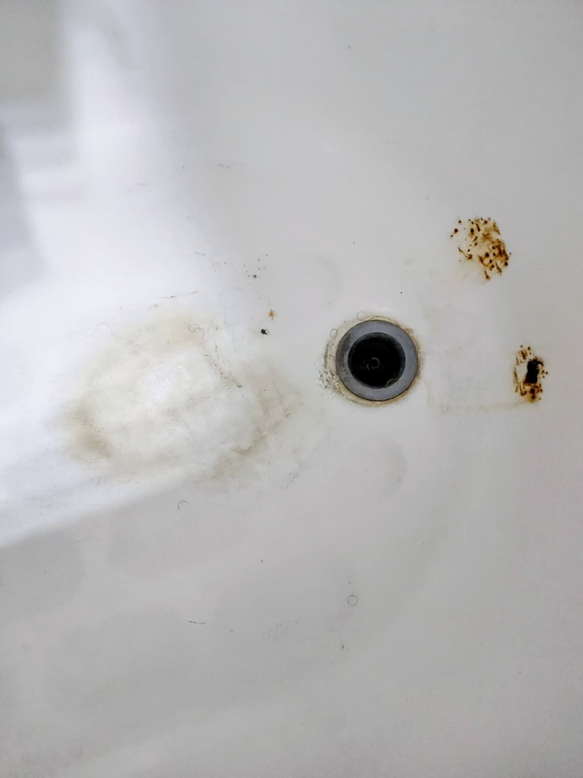 White sink drain with rust stains and a small beige soap residue nearby