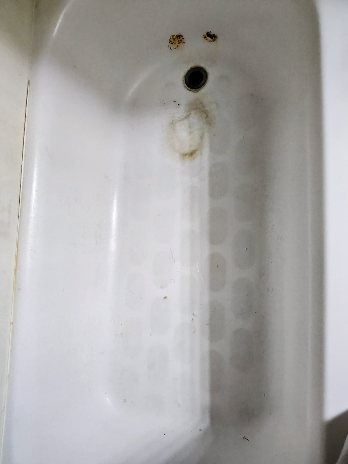 Dirty white bathtub drain with rust stains and grime around the overflow hole