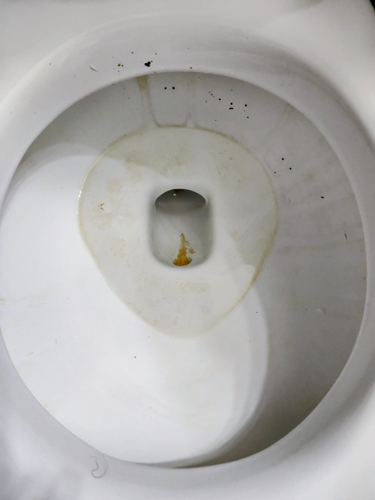 Dirty white toilet bowl with yellow stains and a small amount of residue near the drain.