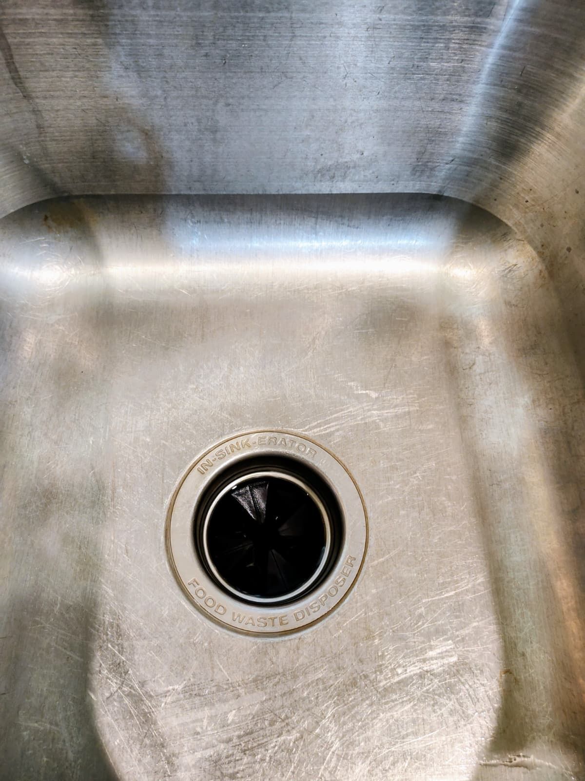 Stainless steel sink basin with a central drain and visible water spots.