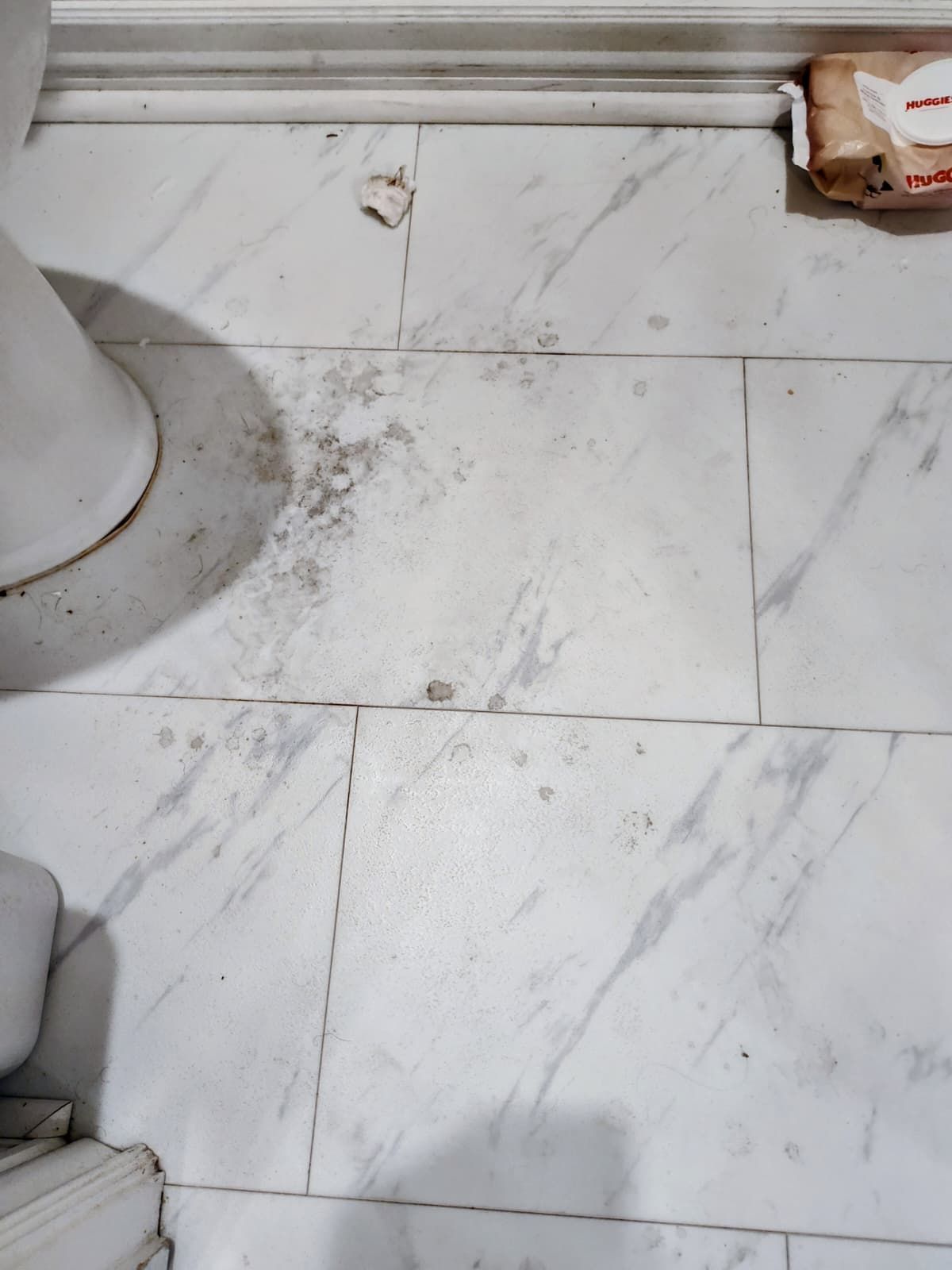 Dusty white tile floor with scuff marks and debris near a baseboard and doorway