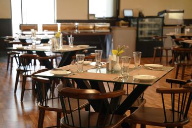 Empty café dining area with wooden tables, chairs, and place settings near large windows