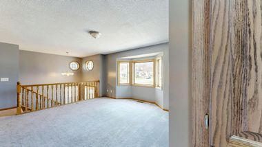 Empty upstairs landing with carpet, staircase railing, gray walls, and a window; close-up of wood door edge.