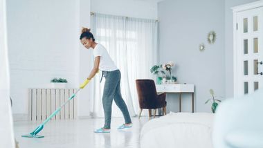 Person mopping a bright white living room with teal mop and bucket