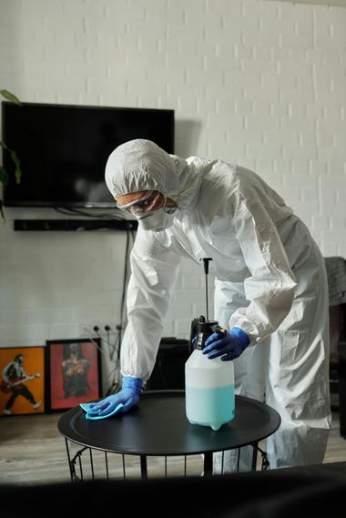 Person in white protective suit pouring blue liquid into a bottle on a table indoors