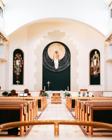 Church sanctuary with wooden pews facing an altar and large religious artwork beneath a vaulted ceiling