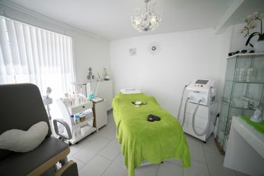 Bright white spa room with green treatment bed, beauty equipment, and cabinet near the window
