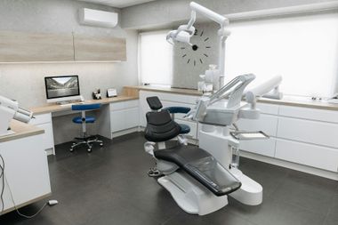 Modern dental exam room with chair, overhead light, computer, and white cabinetry