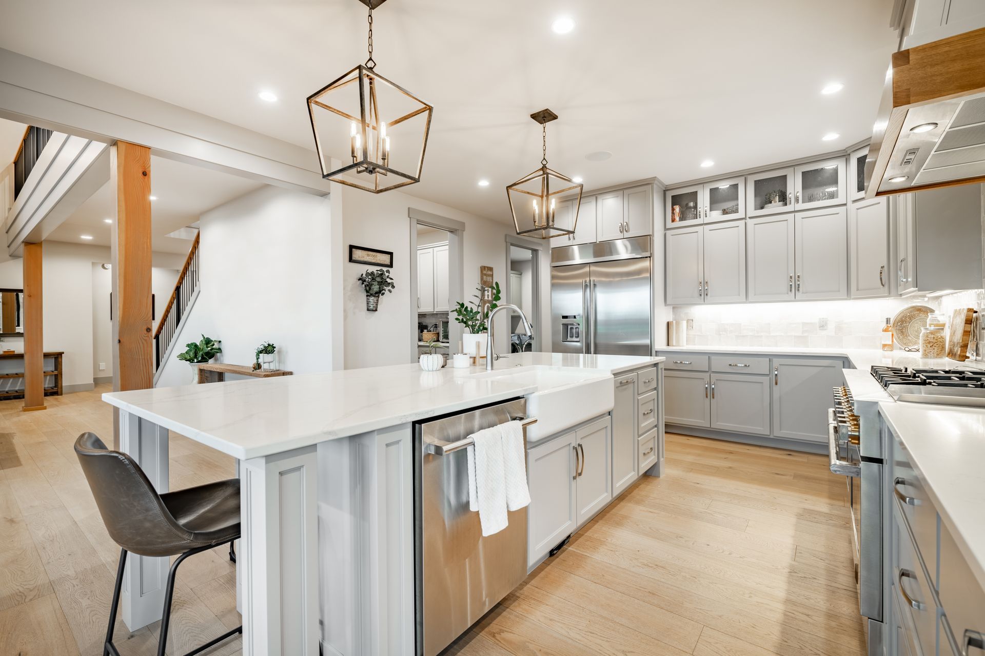 A kitchen with gray cabinets , white counter tops , stainless steel appliances and a large island.