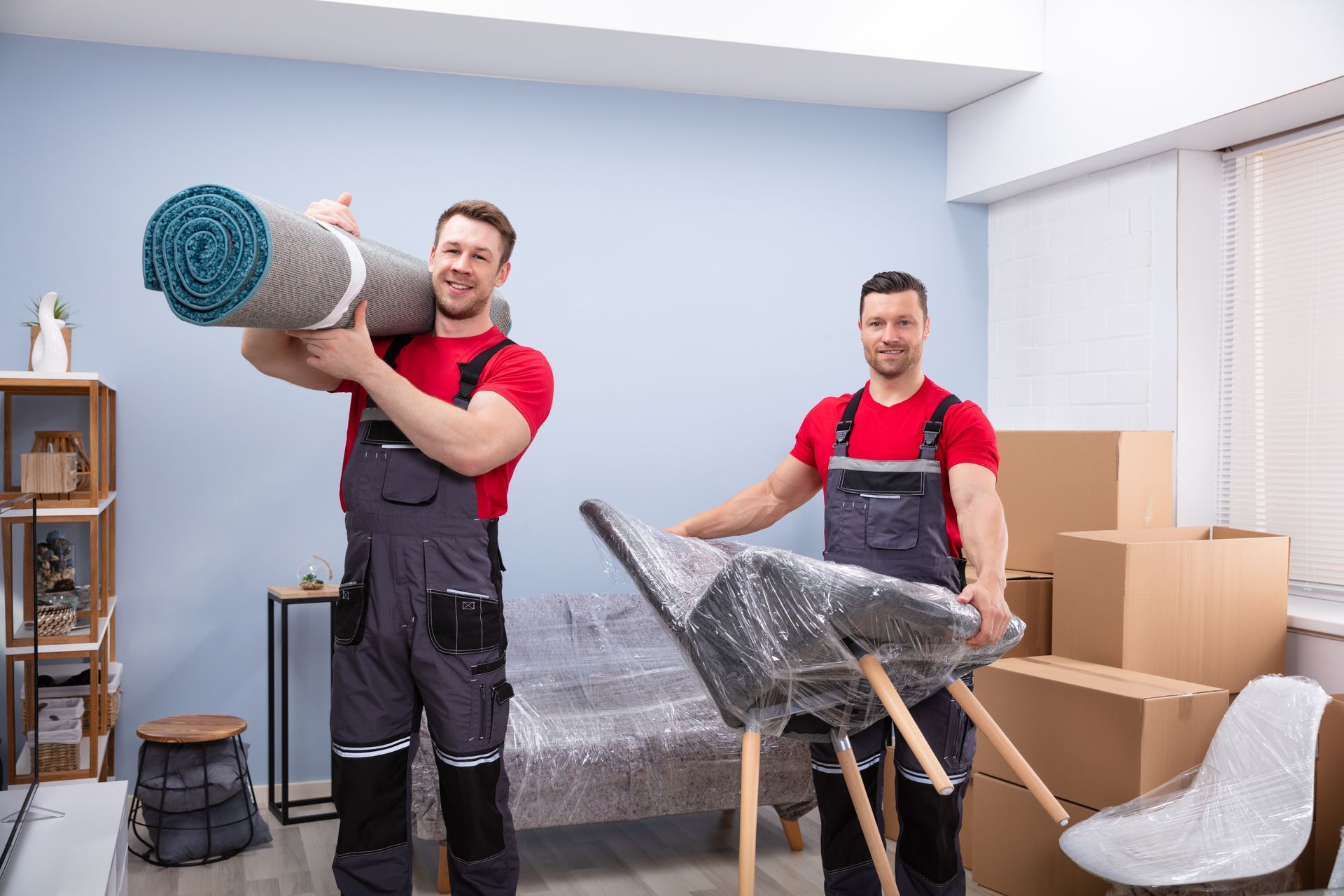 Two men are moving a chair and a rug in a living room.