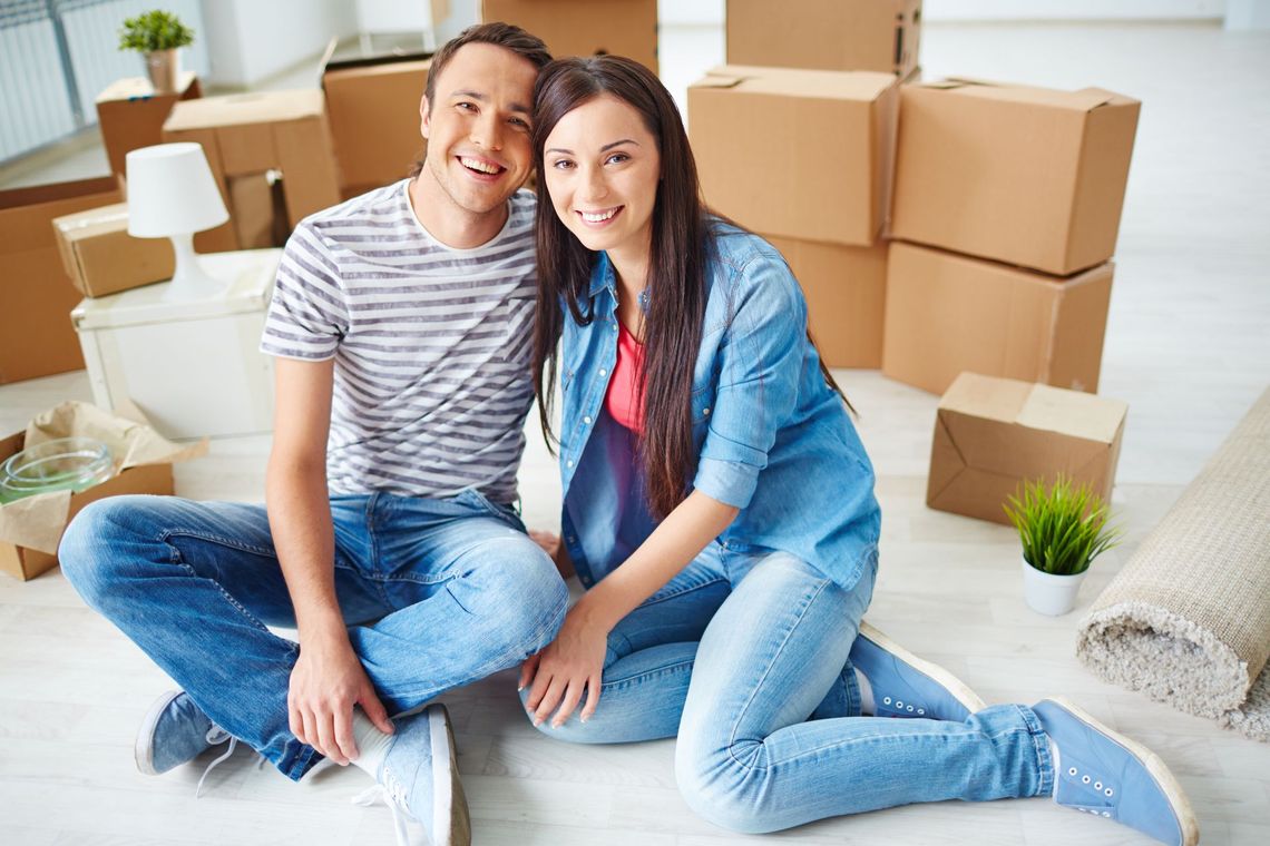 A man and a woman are sitting on the floor in front of moving boxes.