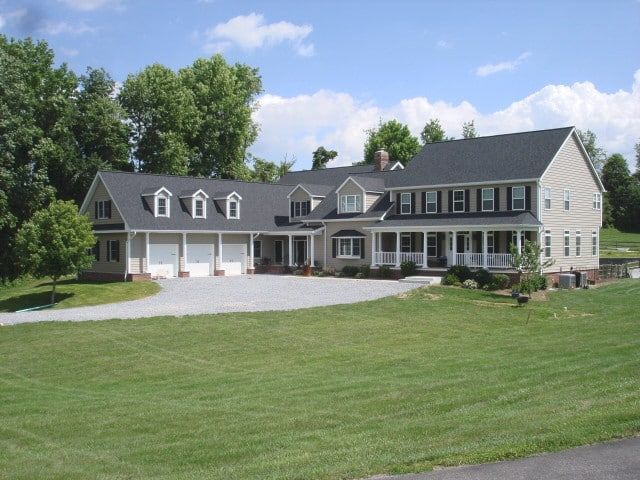 Large gray suburban house with white garage doors and a wide green lawn under a partly cloudy sky