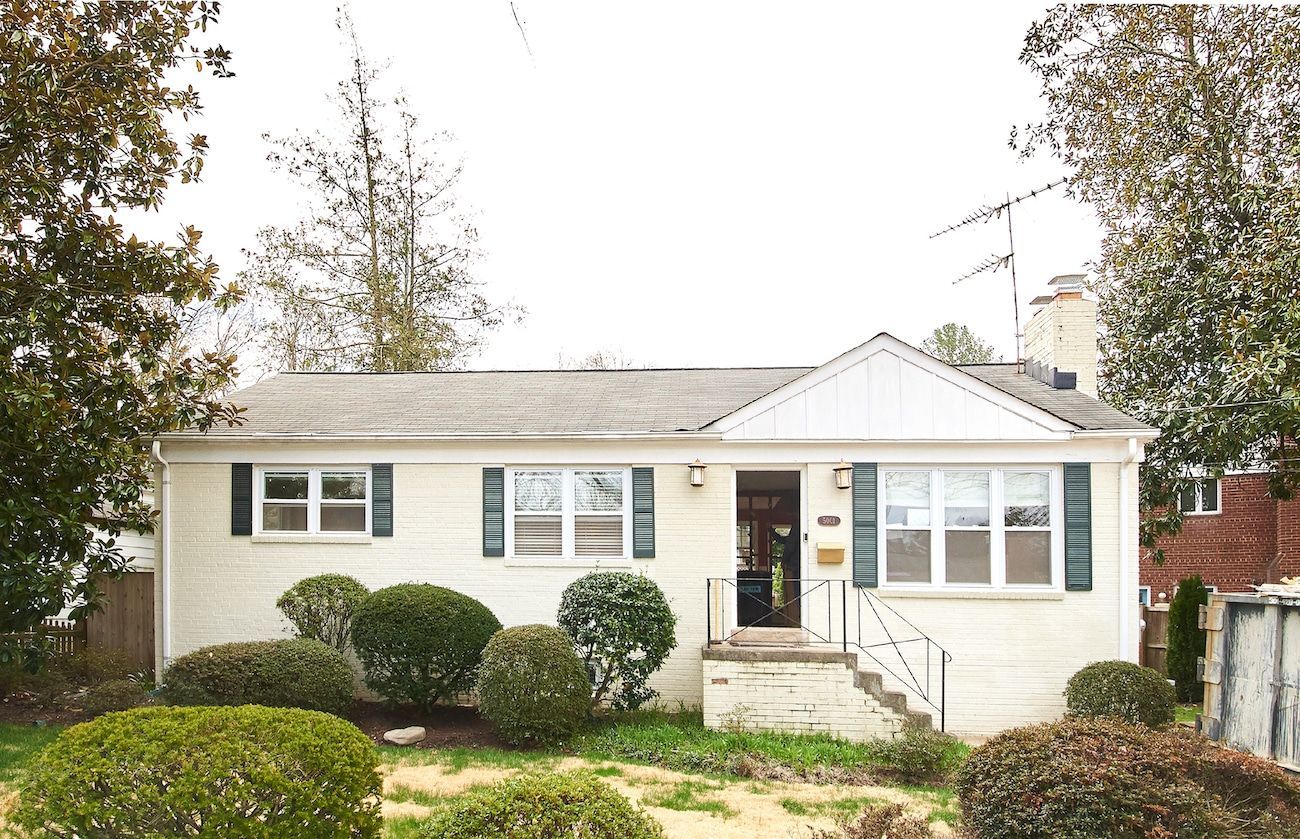Single-story white house with front steps, trimmed shrubs, and a small front yard