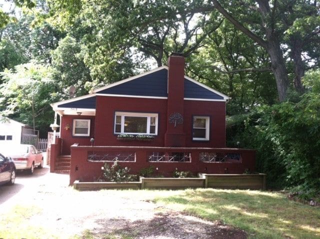 Small red house with a front porch and chimney surrounded by trees