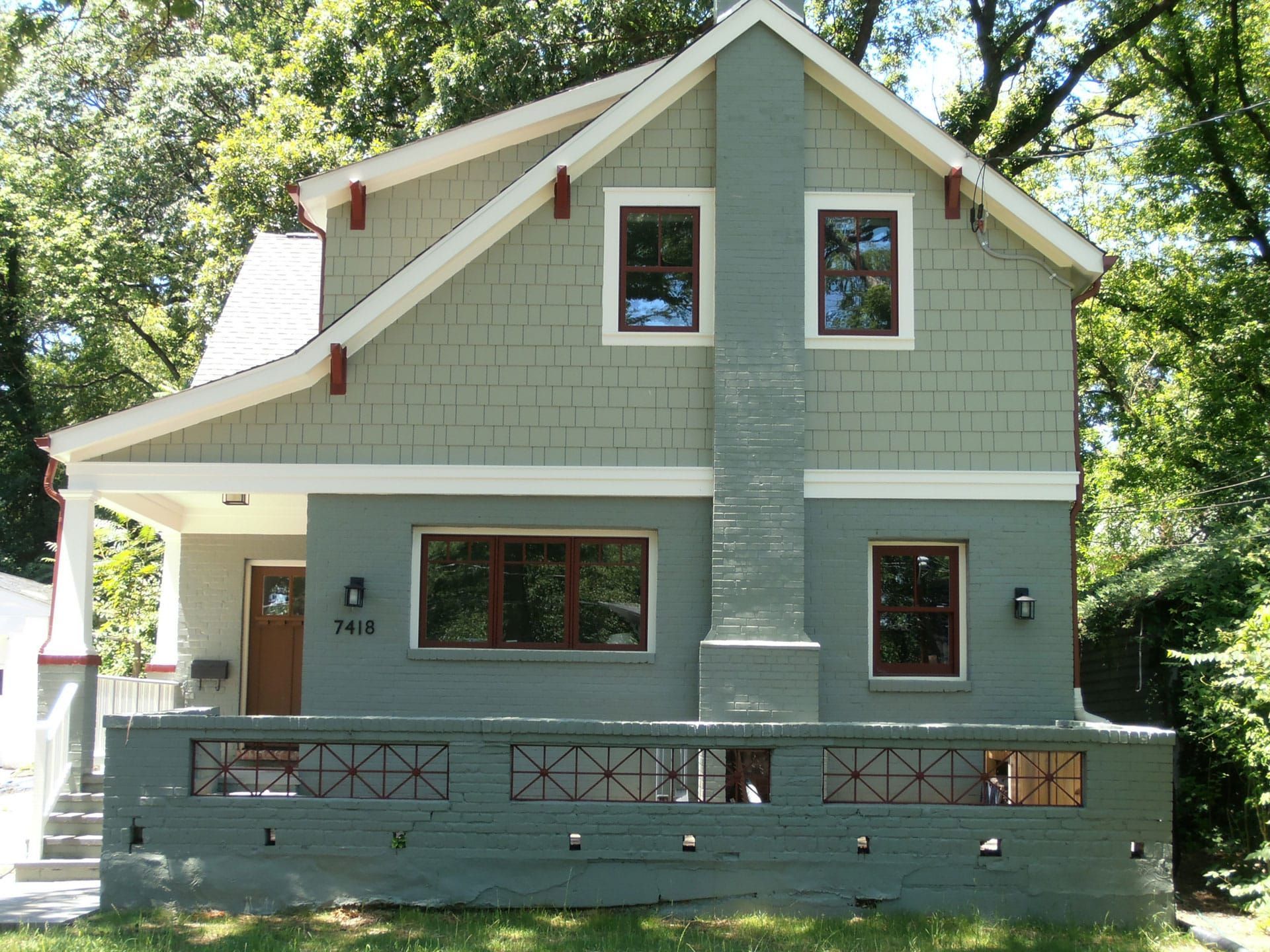 Green two-story house with gray trim, front porch, and trees in the background