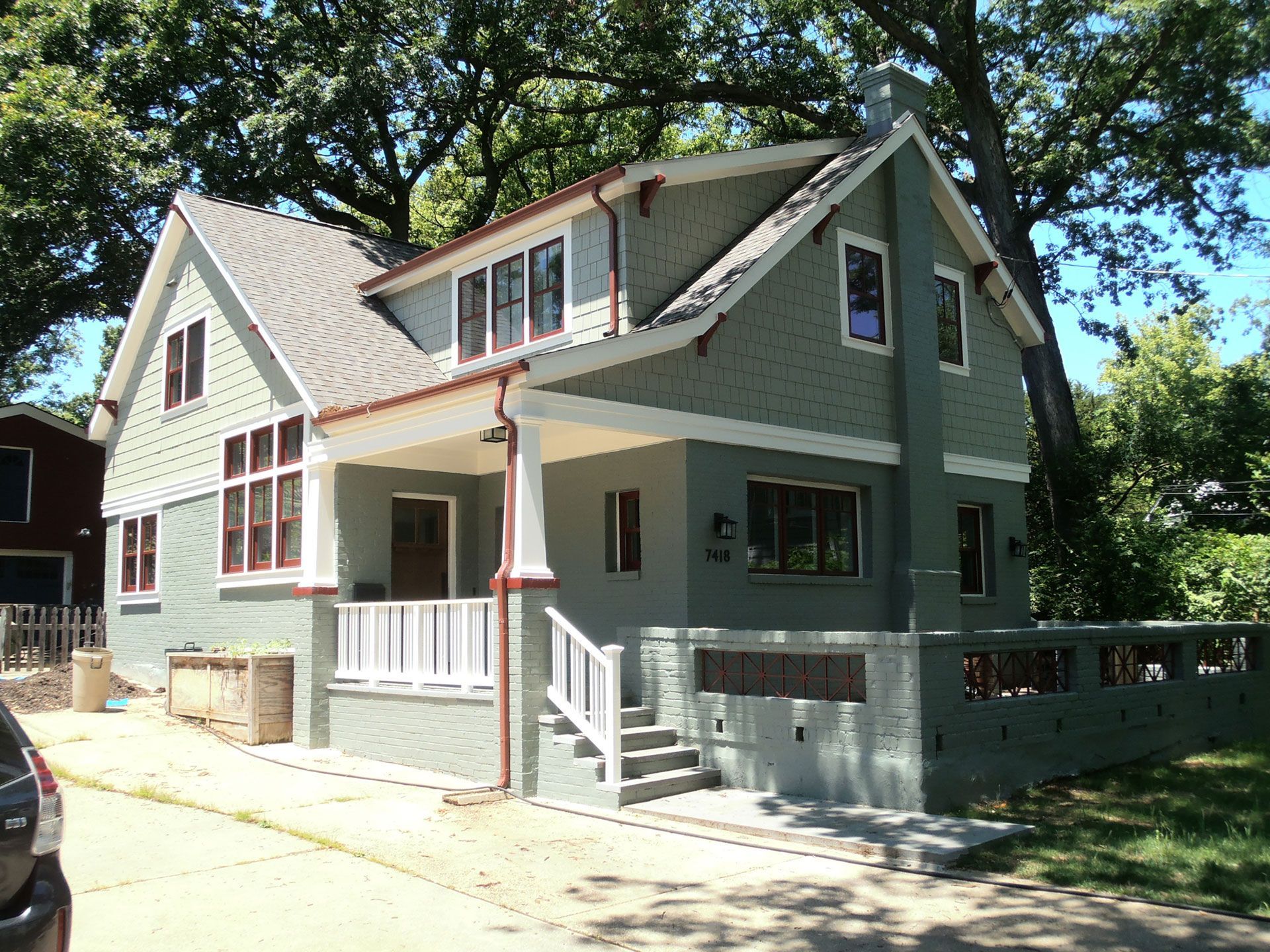 Gray-green house with white trim, front porch, and stair railing on a sunny street.