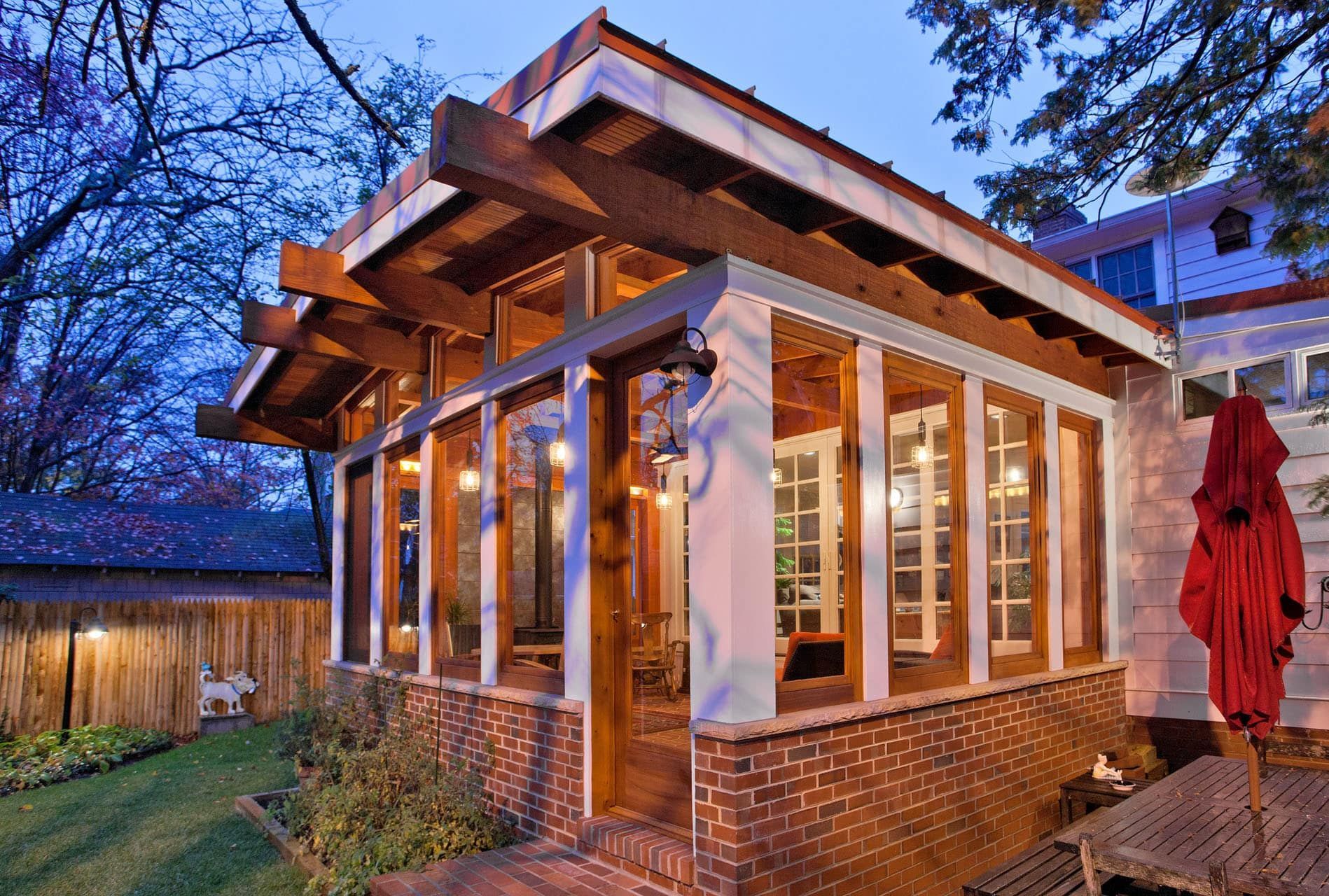 Brick sunroom with large windows and exposed beams beside a patio at dusk