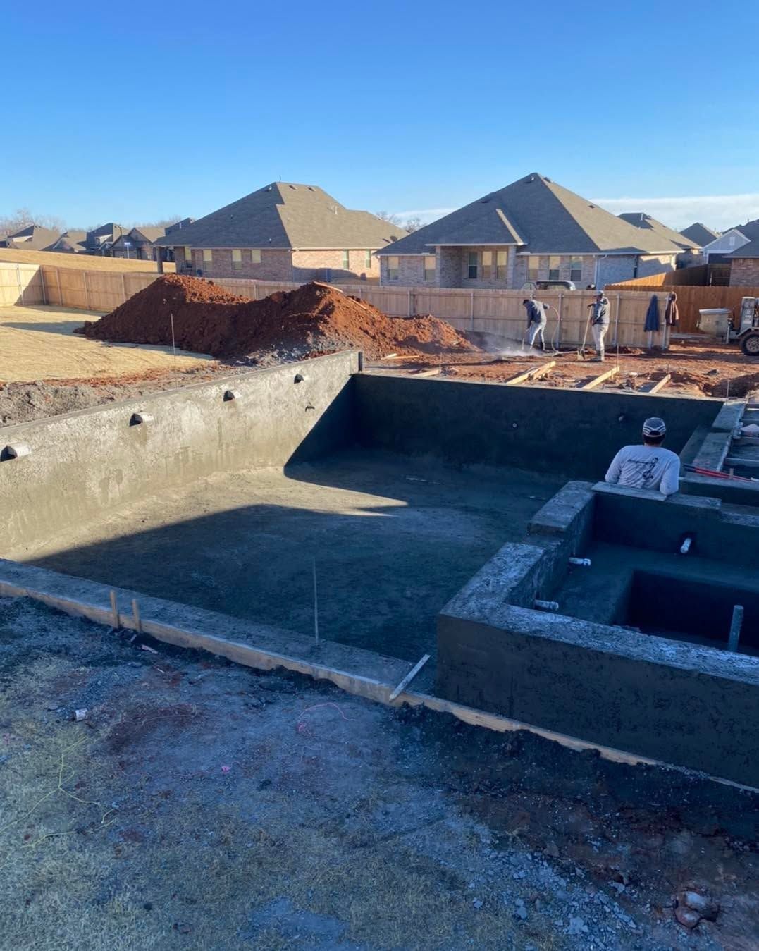 Construction site foundation pits with concrete walls and a worker in a hard hat under a clear sky.