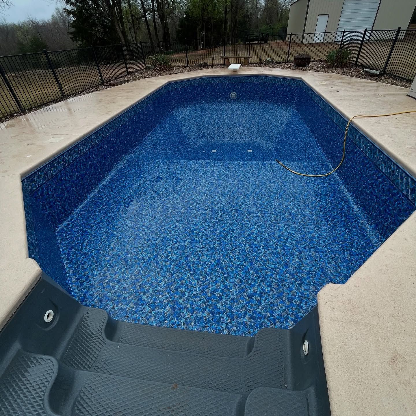 Backyard pool with blue water and a gray pool step in the foreground