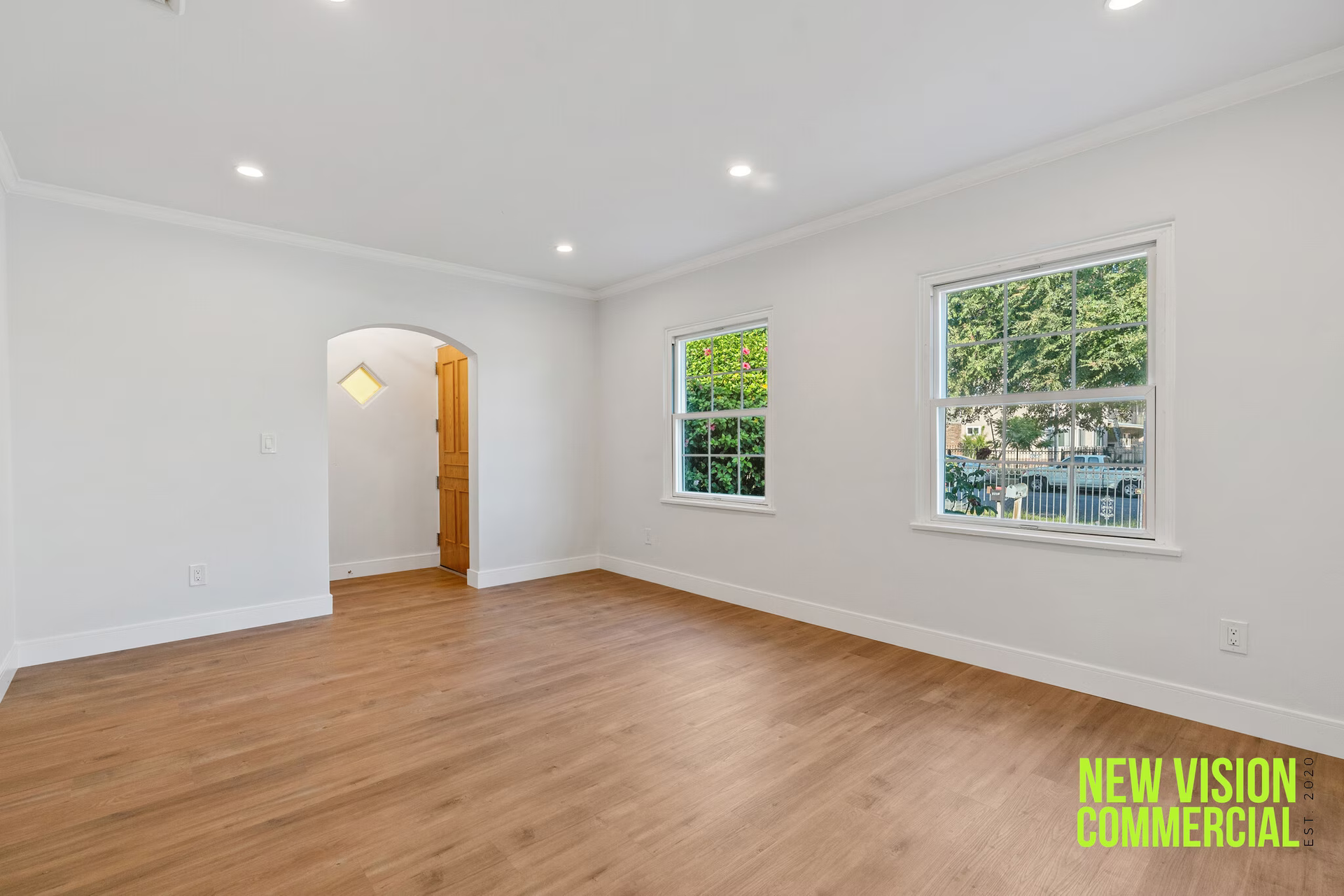 An empty living room with hardwood floors and two windows.
