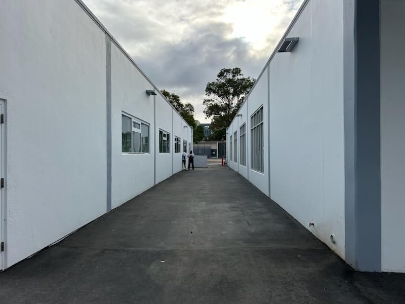Narrow walkway between two white buildings. Two figures walk towards the end, under cloudy sky.