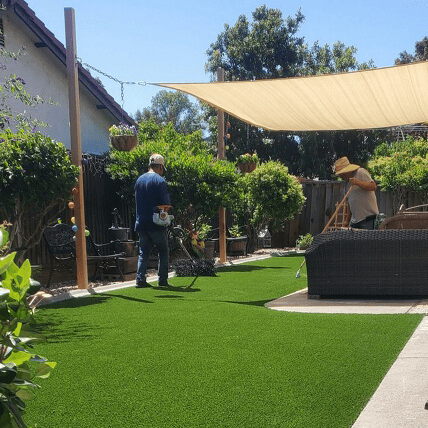 Two men working in a sunny backyard. A shade sail provides cover.