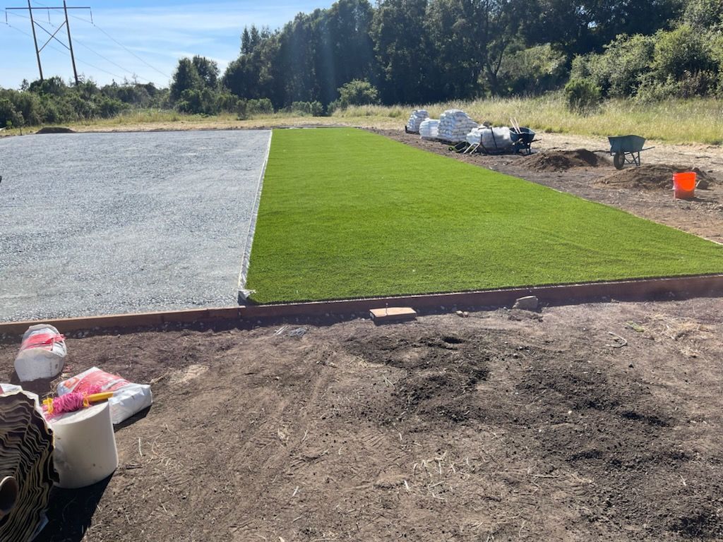A section of artificial turf next to a gravel area, with supplies nearby.