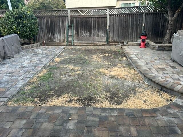Backyard with brick patio surrounding a patch of bare dirt, a fence, and a red fire hydrant.