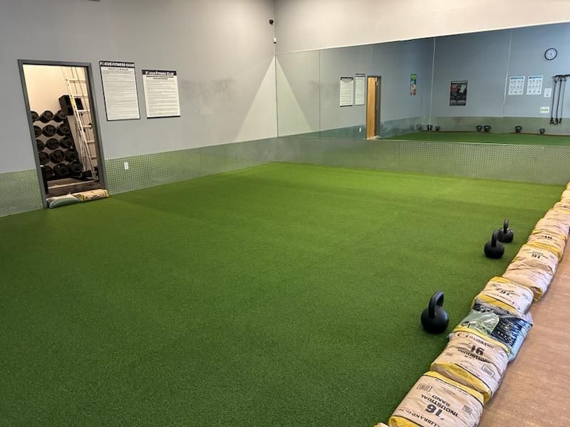 Gym interior with green turf, weights, and a large mirror.