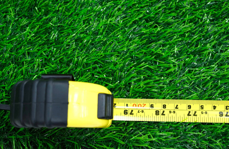 Yellow tape measure extending over green artificial grass.