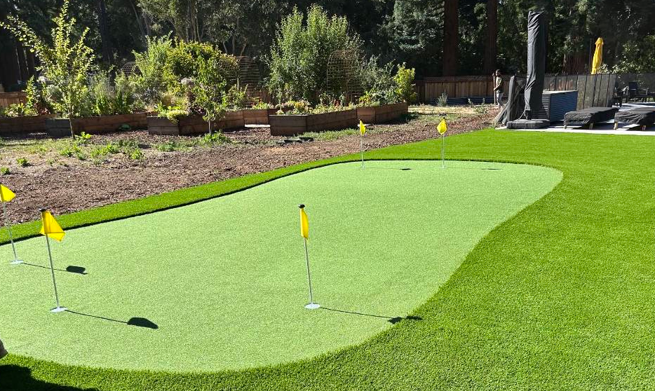 A well-manicured putting green with yellow flags set on artificial turf in a backyard.