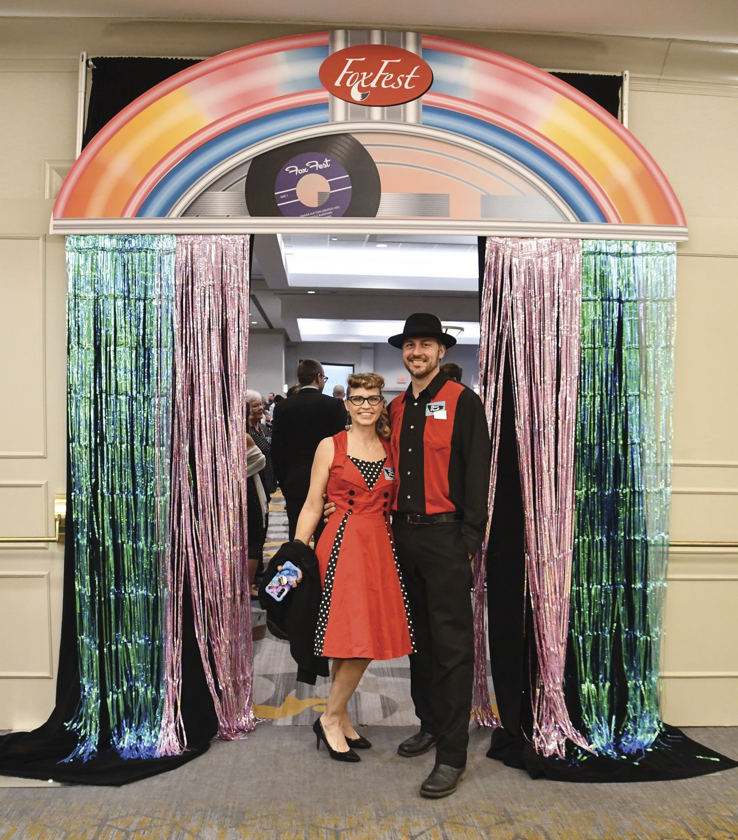 Couple dressed in 50s clothing, smiling and standing in the jukebox entrance to the event
