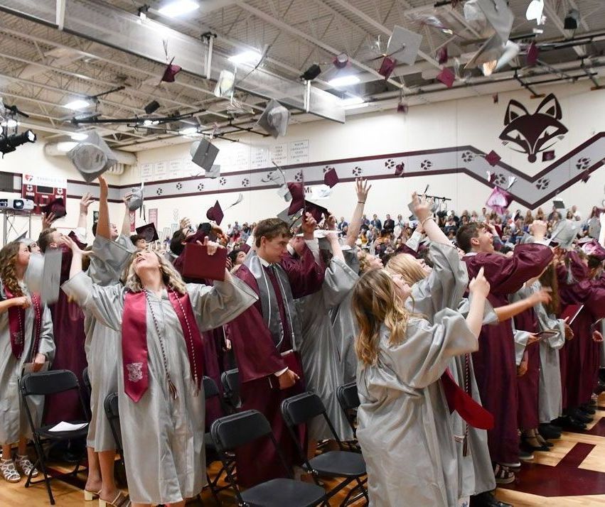 Seniors standing in their places in the gym, tossing their mortar boards in the air after they all graduated