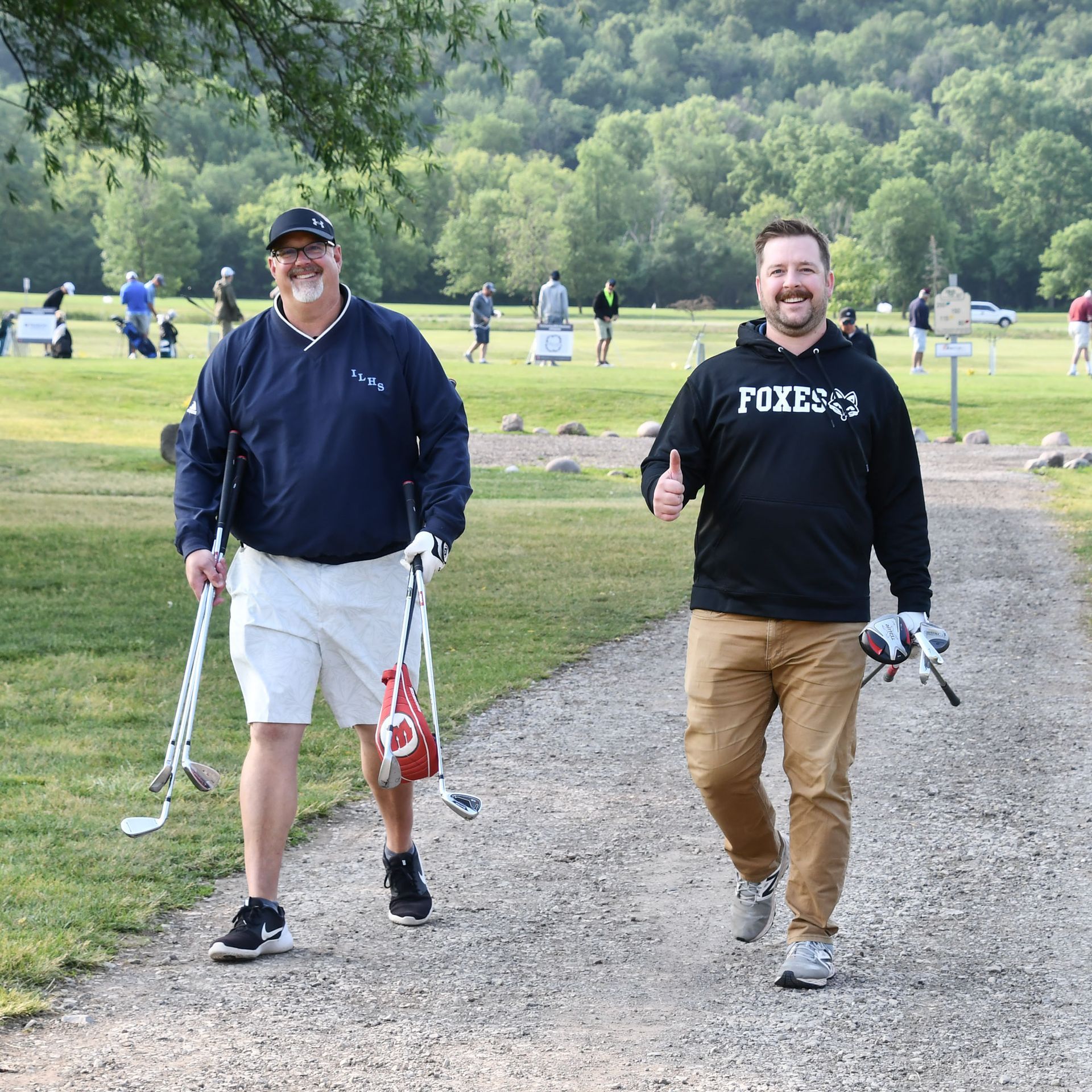 Mr. Uhlenbrauck and Mr. Dorn walking on the path, smiling and carrying golf clubs.