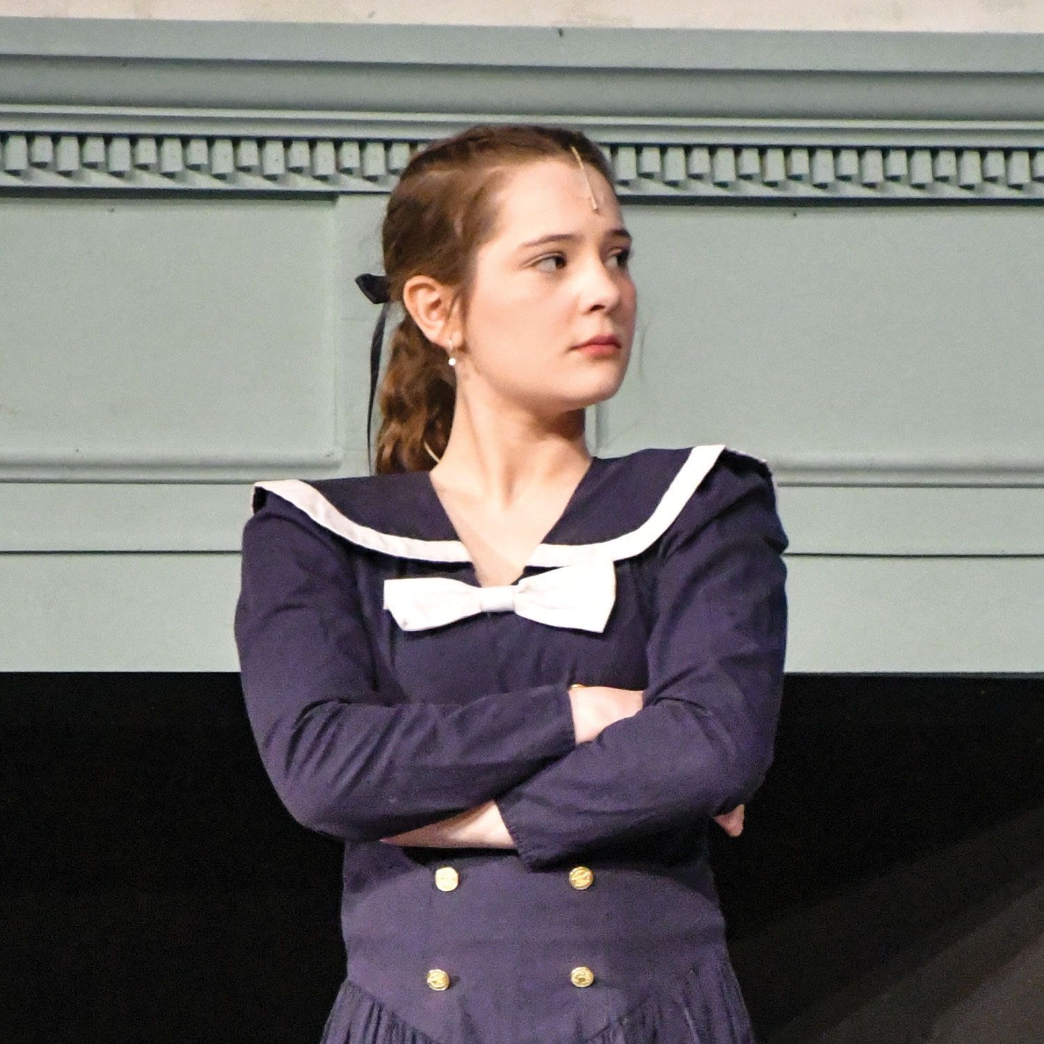Grace Peters as Jane Banks, standing in front of the family's fireplace.