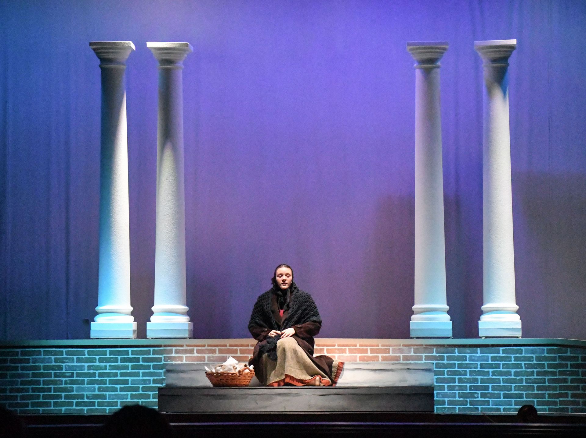 Old woman sitting on steps with pillars behind her.