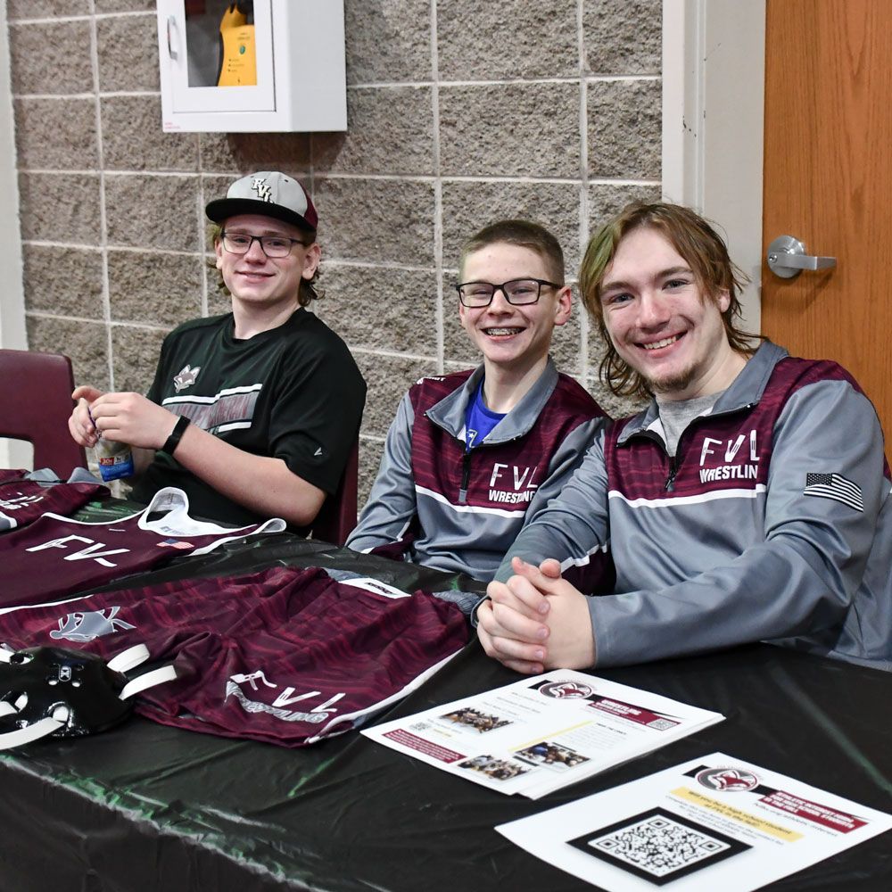 Three wrestling students at their table, ready to talk to visitors about the team