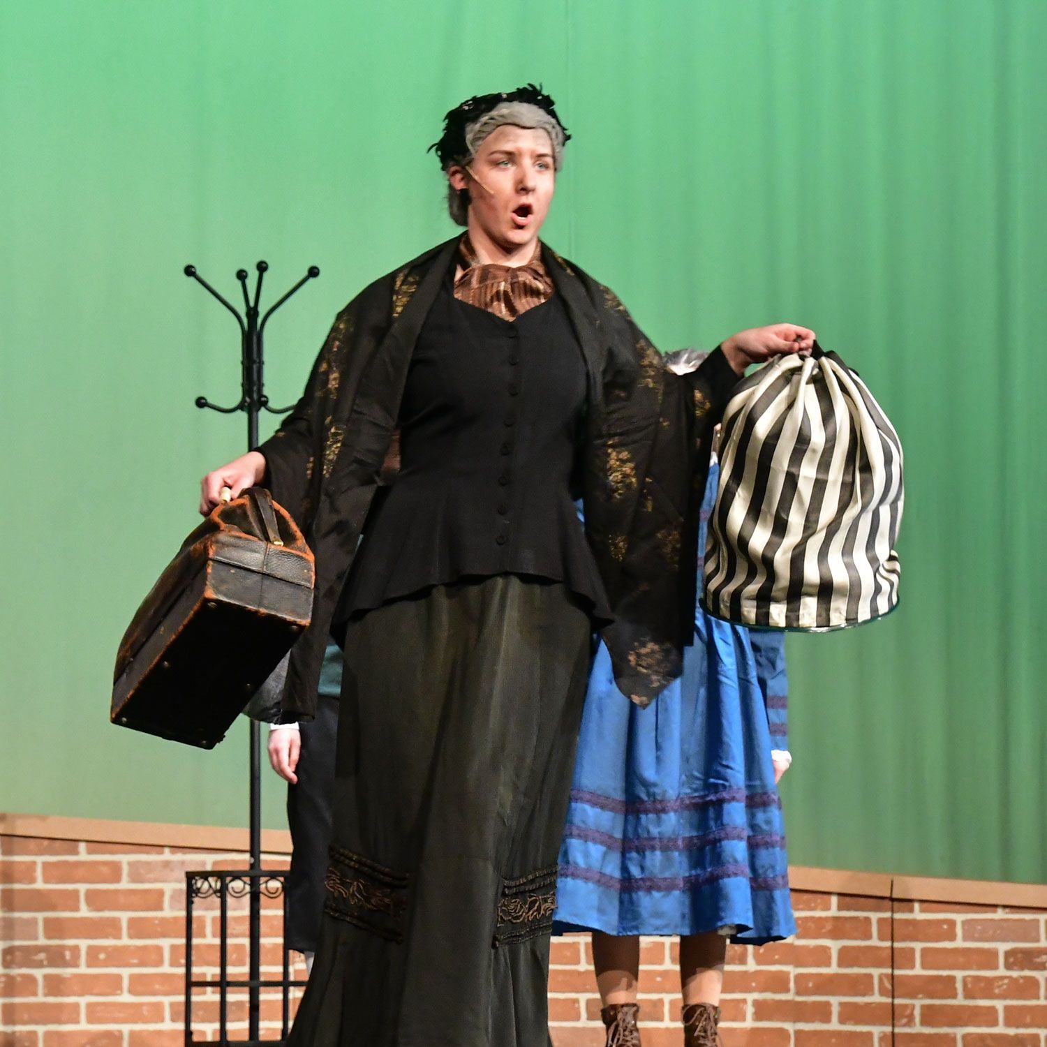 Ellason Popp as Miss Andrew, holding a covered birdcage and her bag of belongings.