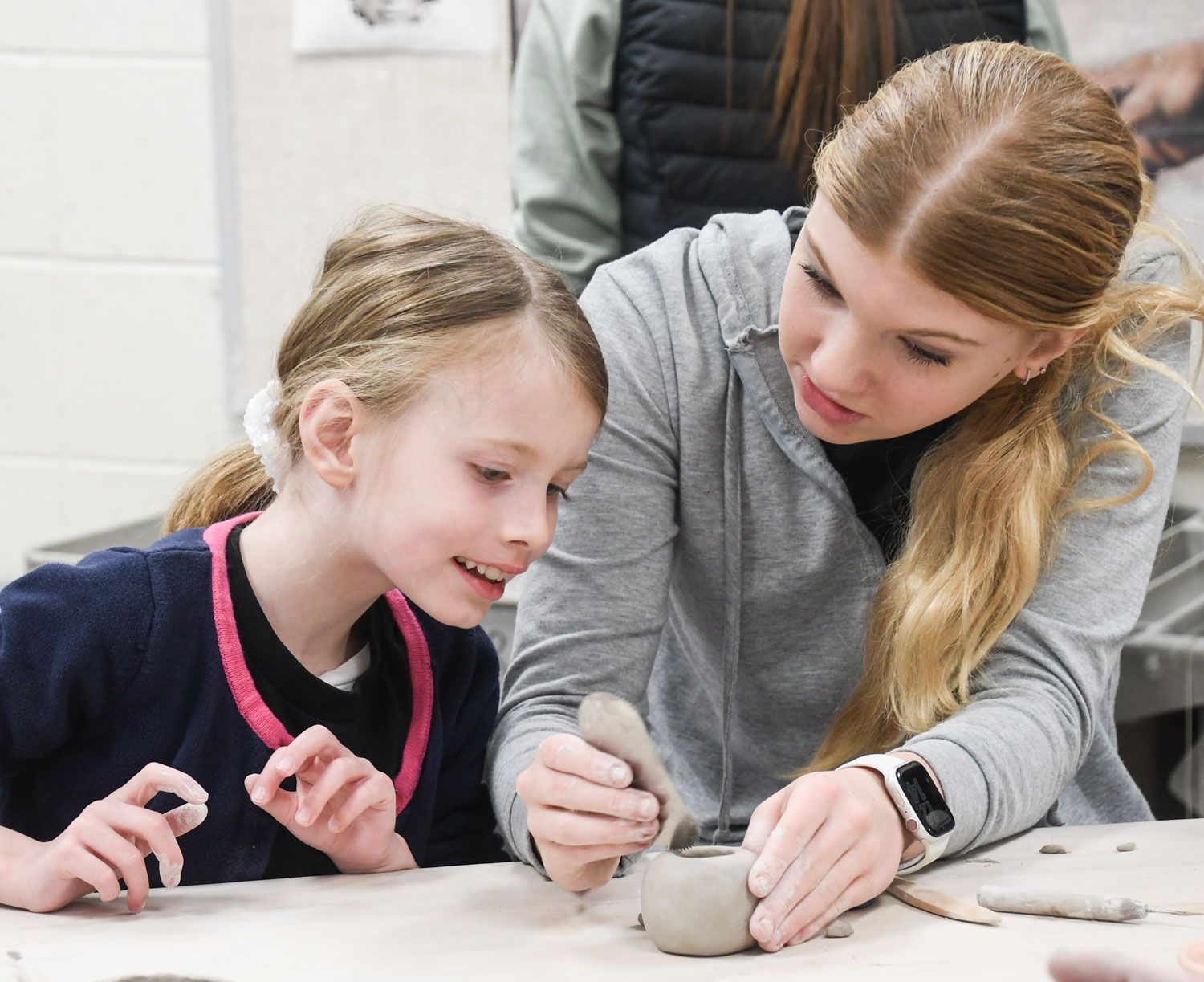 High school girl is working with an elementary student on a ceramics project.