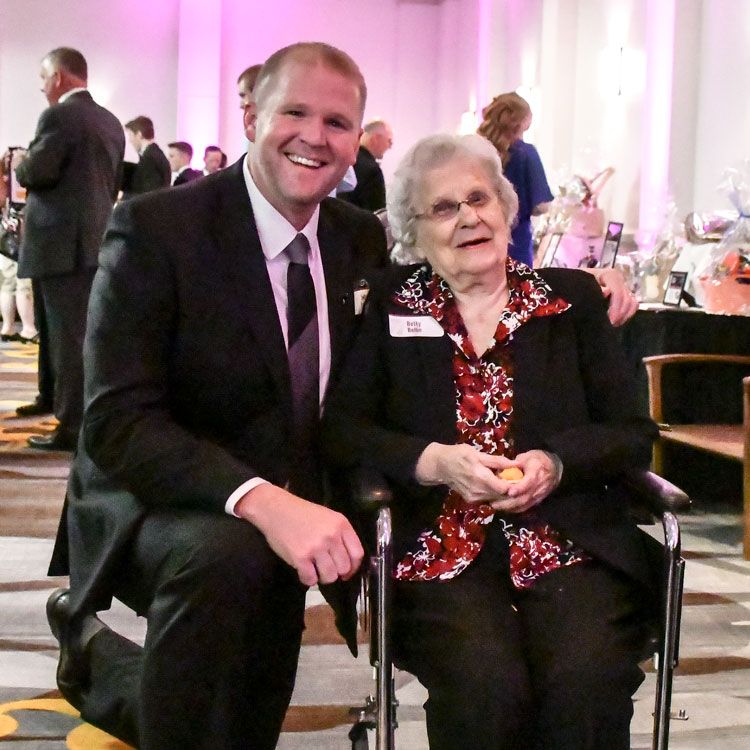 Jeff Loberger kneeling by a 100-year-old guest in a wheelchair at the Dinner Auction