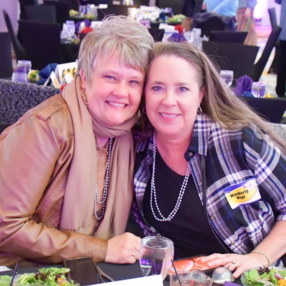 Two smiling women at a dinner table at last year's event